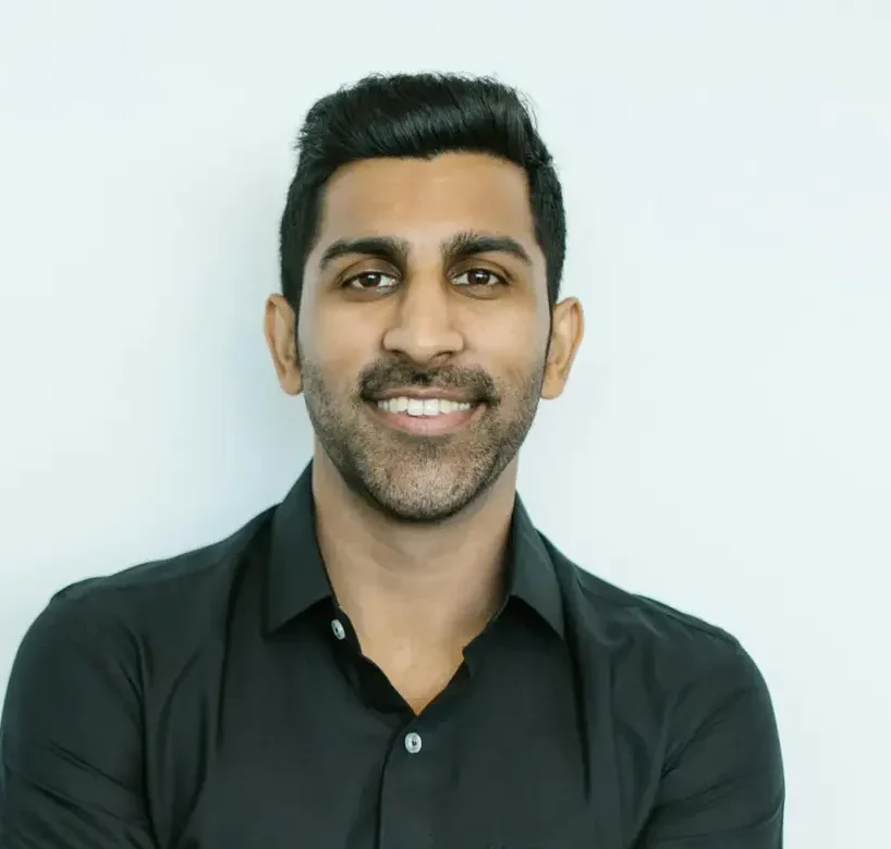Portrait of a confident man in black shirt smiling against a plain background.